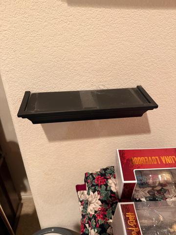 A dusted floating wall shelf in a lived-in home.