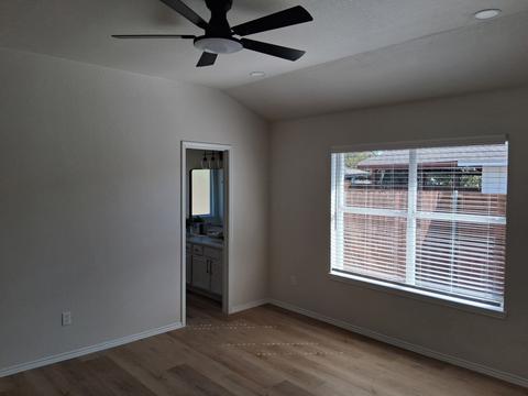 An empty bedroom with a ceiling fan, window and freshly cleaned floor.