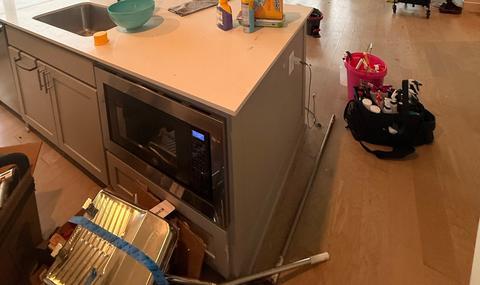 A kitchen island mid-clean, with cleaning supplies and a supply caddy on the floor.